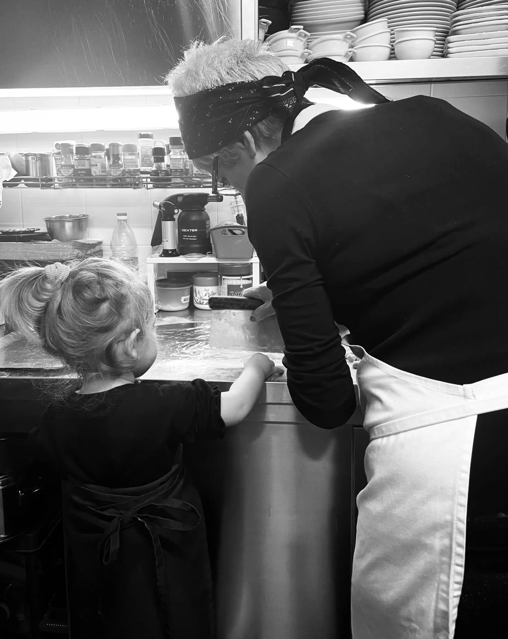 Black and white image of an elderly woman and a young kid cooking together